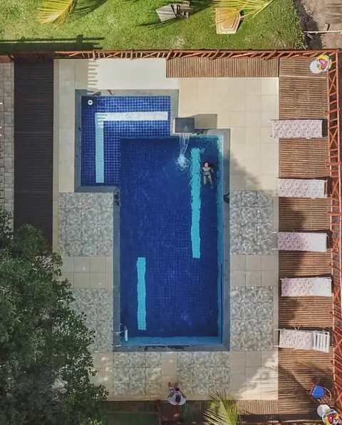 Vista de drone da piscina, deck de madeira e área de descanso.
