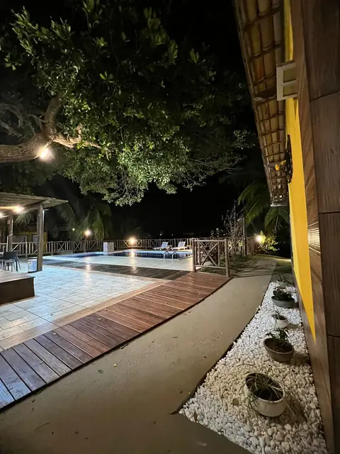 Deck de madeira, luzes quentes e a copa da amendoeira emoldurando a piscina.